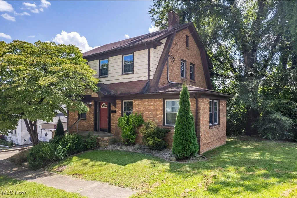 View of front facade with brick siding, a front lawn, a chimney, and a gambrel roof