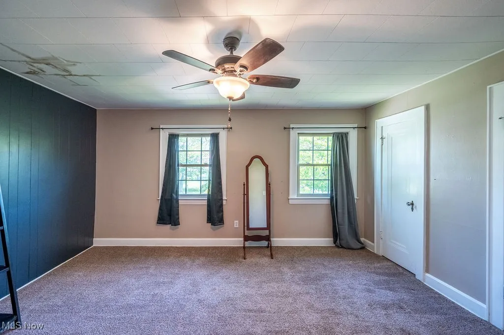Unfurnished bedroom featuring carpet flooring, multiple windows, ceiling fan, and wood walls