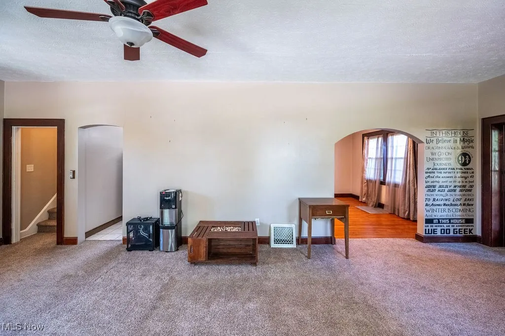 Carpeted spare room featuring arched walkways, a textured ceiling, stairway, and ceiling fan