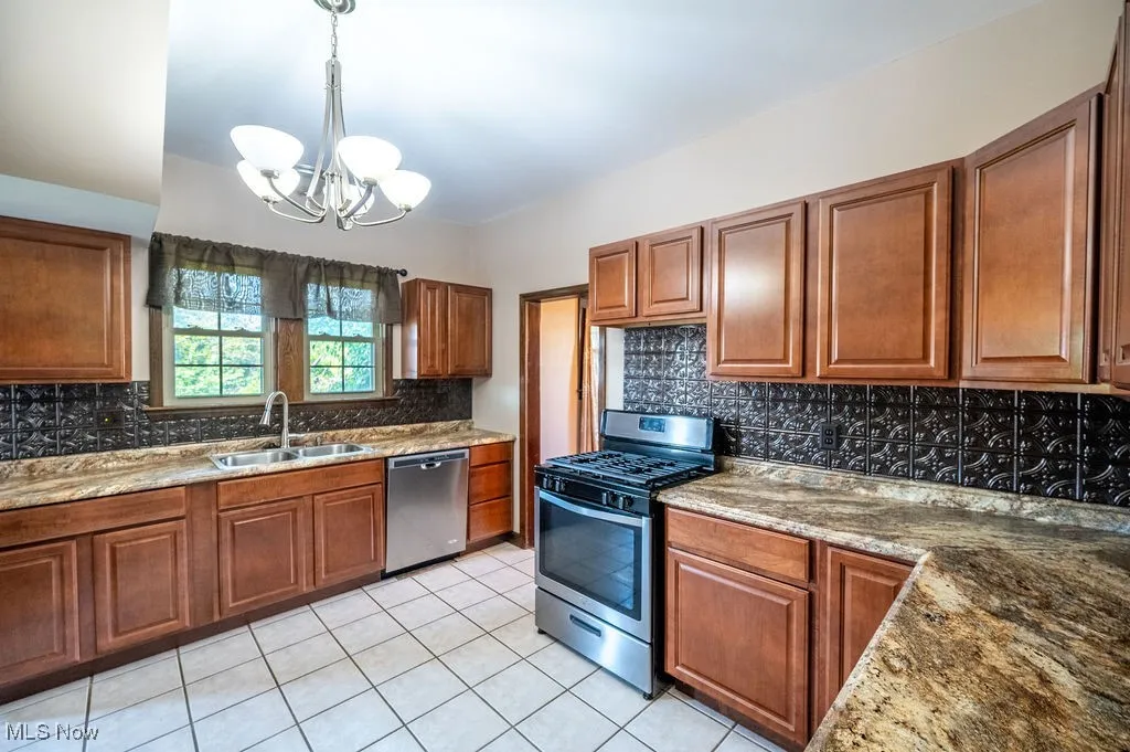 Kitchen with stainless steel appliances, brown cabinetry, tasteful backsplash, a chandelier, and light tile patterned floors