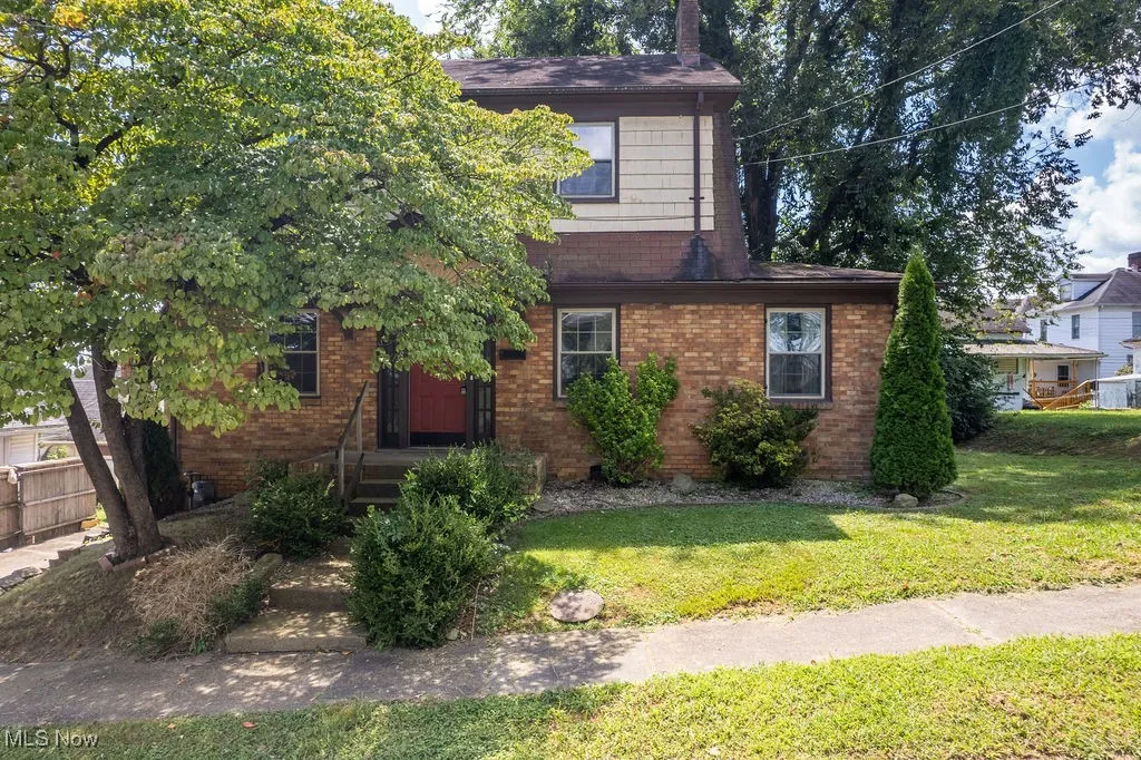 View of front facade featuring brick siding, roof with shingles, and a front yard