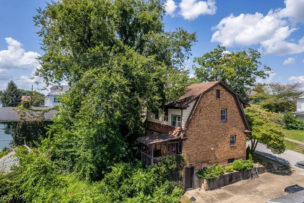 View of side of property with a gambrel roof, brick siding, and a balcony