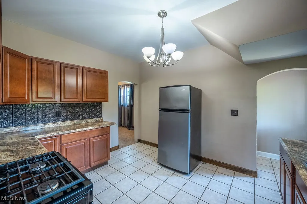 Kitchen featuring arched walkways, freestanding refrigerator, decorative backsplash, gas stove, and pendant lighting