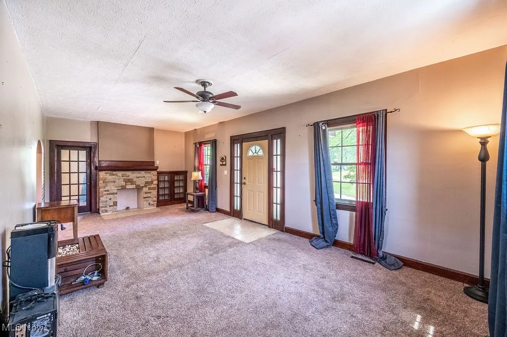 Unfurnished living room featuring carpet flooring, ceiling fan, a textured ceiling, and a fireplace