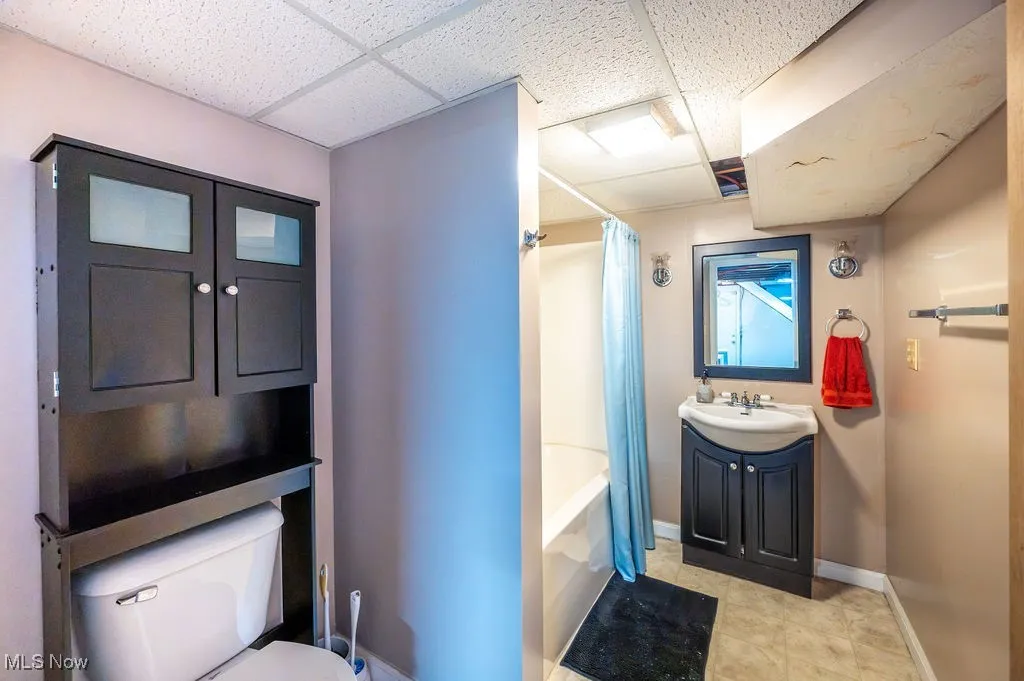 Bathroom featuring shower / bath combo with shower curtain, vanity, a drop ceiling, and light tile patterned floors