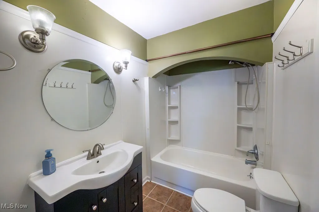 Bathroom featuring vanity, shower / tub combination, and dark tile patterned flooring