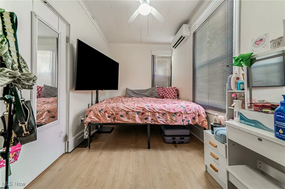 Bedroom with light wood-style flooring, crown molding, a ceiling fan, a wall mounted AC, and multiple windows