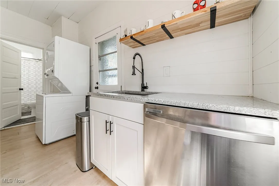 Kitchen featuring dishwasher, white cabinetry, estacked washer and dryer, light wood-type flooring, and light stone counters