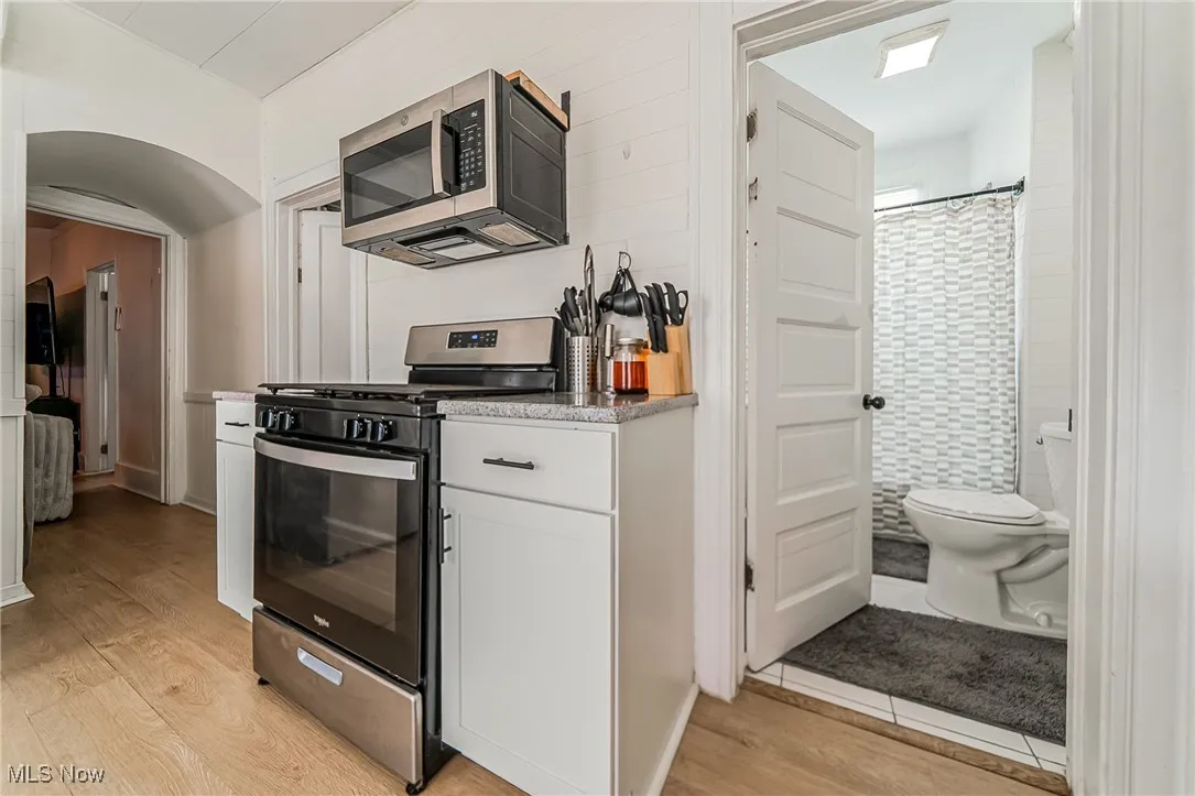 Kitchen with appliances with stainless steel finishes, white cabinetry, arched walkways, and light wood-style floors