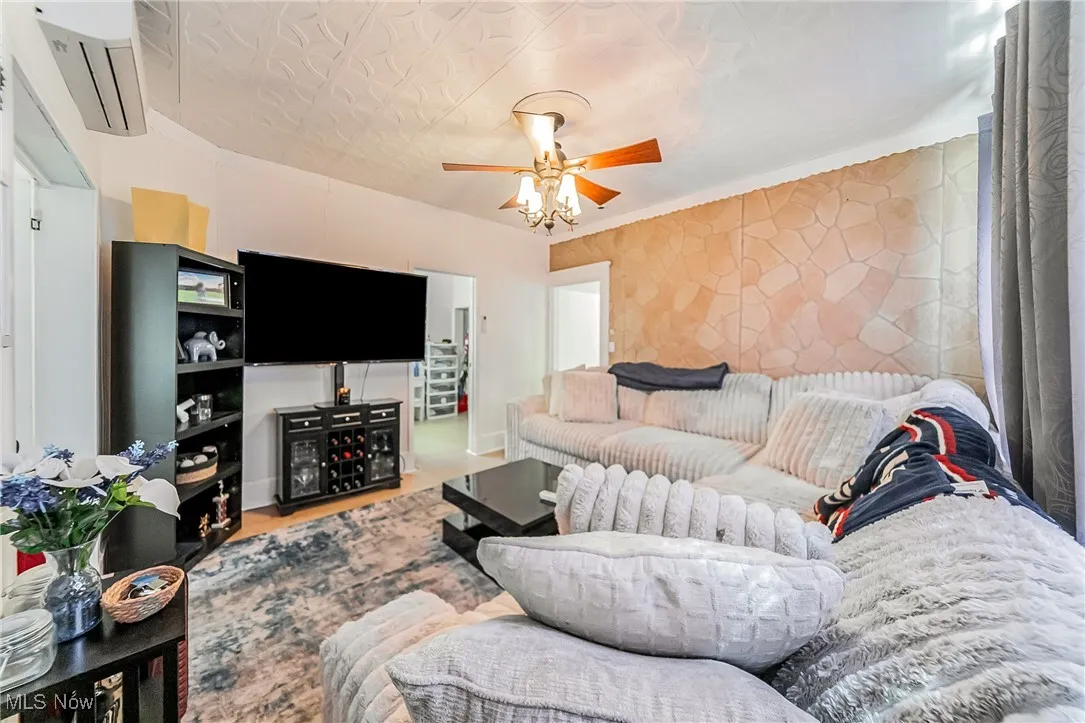 Living area with an ornate ceiling, a wall unit AC, and ceiling fan