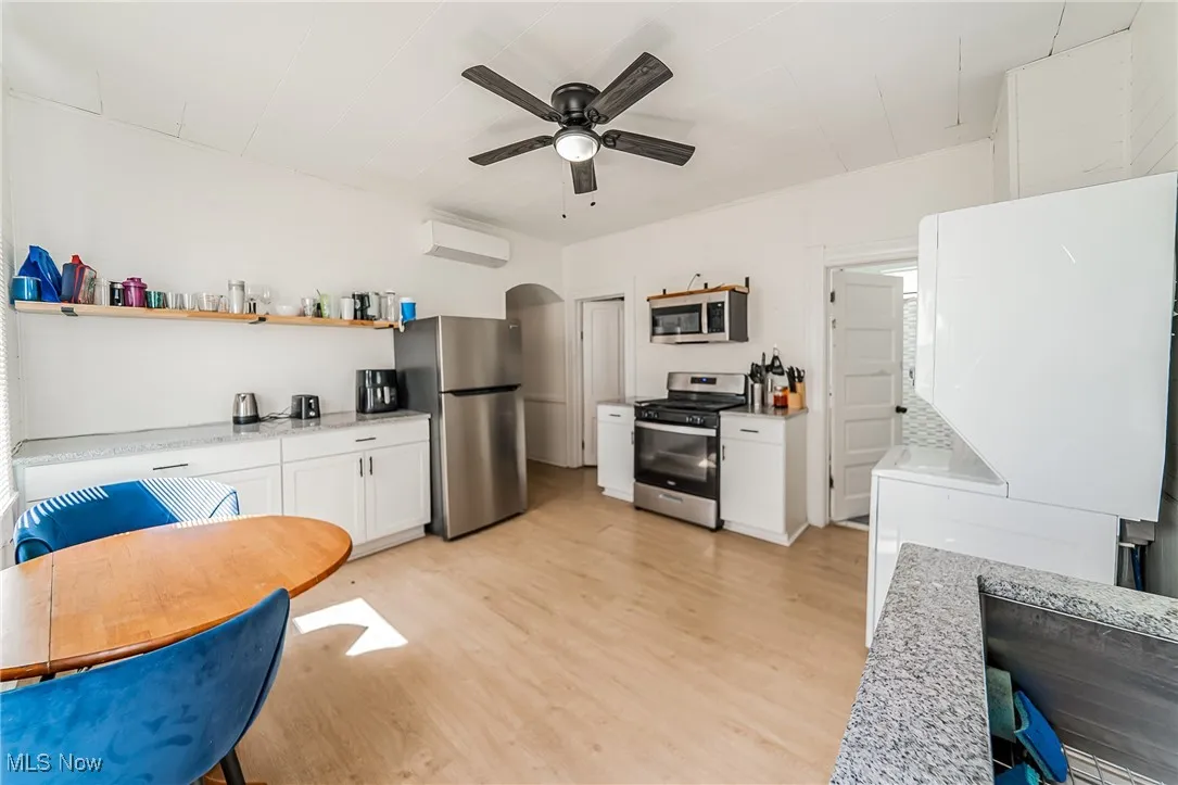 Kitchen featuring stainless steel appliances, white cabinetry, arched walkways, light wood-style floors, and open shelves