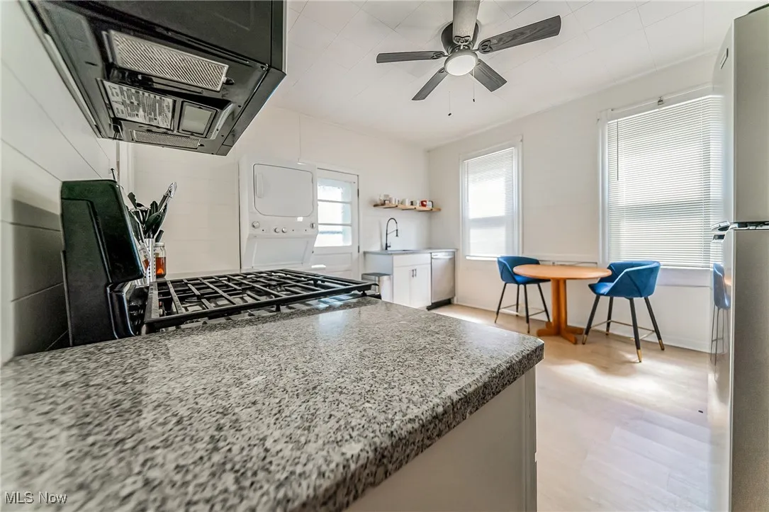 Kitchen with ventilation hood, stainless steel appliances, light stone counters, ceiling fan, and estacked washer and dryer