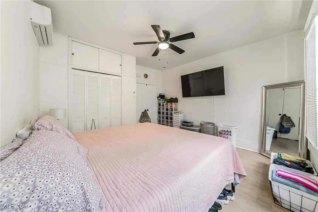 Bedroom with a closet, light wood finished floors, a wall mounted AC, and a ceiling fan