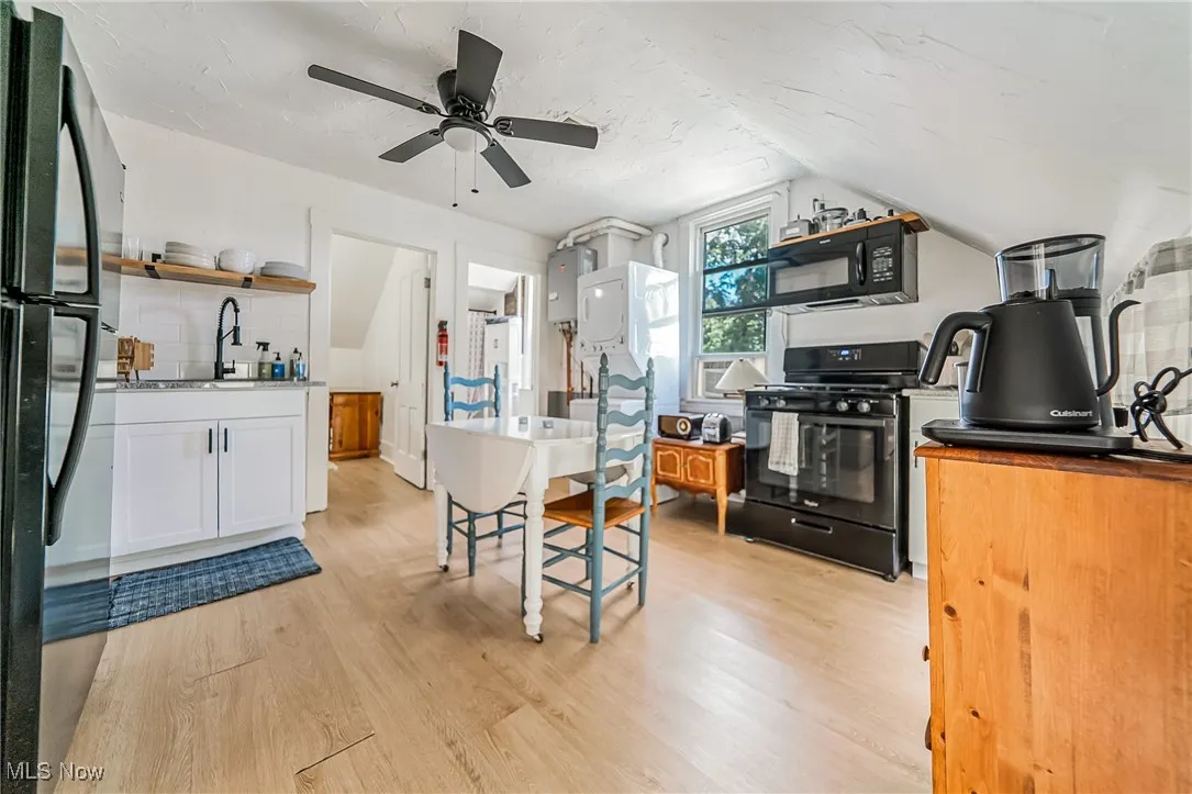 Kitchen with black appliances, light wood-style flooring, white cabinetry, water heater, and open shelves