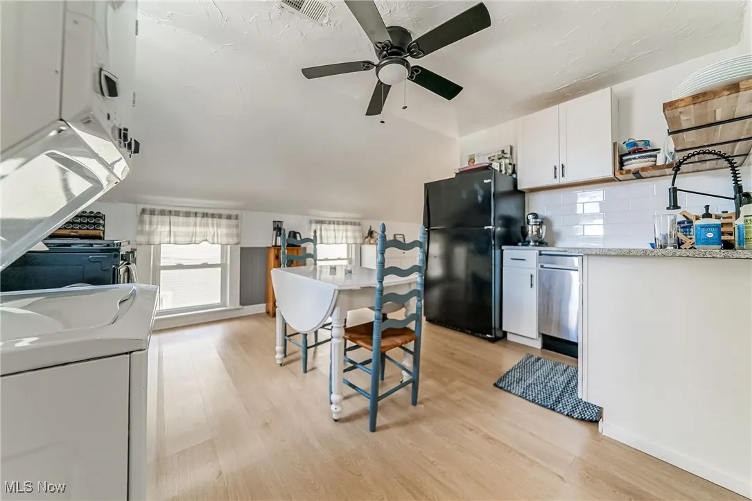 Kitchen featuring white cabinets, light wood-type flooring, freestanding refrigerator, decorative backsplash, and washer / clothes dryer