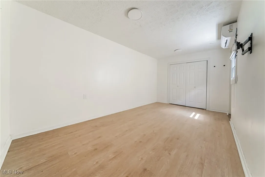 Unfurnished bedroom with light wood-type flooring, a textured ceiling, an AC wall unit, and a closet