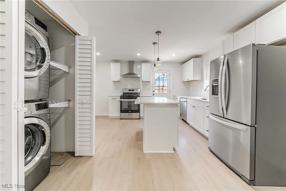 Kitchen with appliances with stainless steel finishes, light countertops, light wood-style flooring, white cabinets, and hanging light fixtures