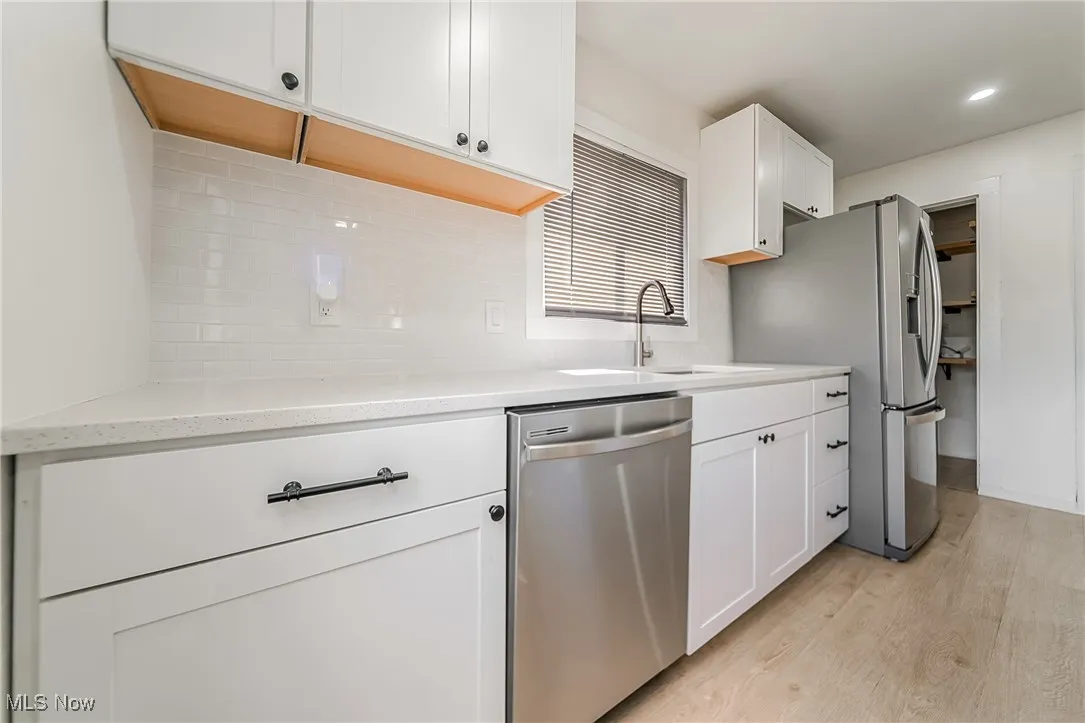 Kitchen with white cabinetry, appliances with stainless steel finishes, light wood-type flooring, decorative backsplash, and light stone counters