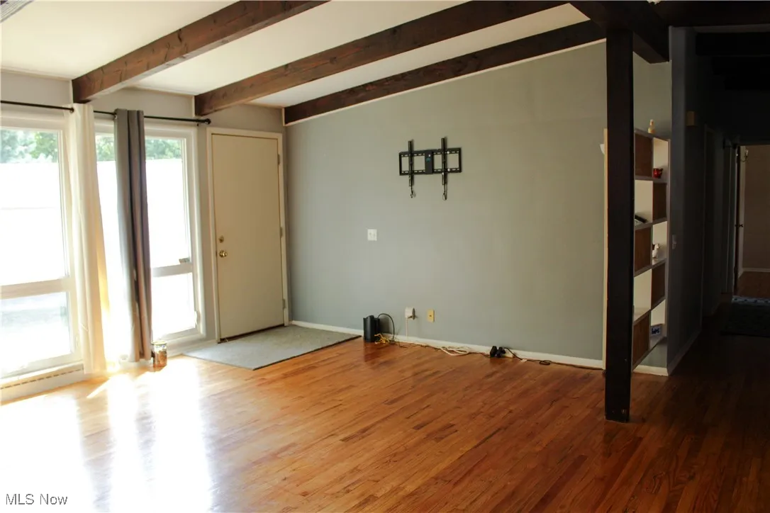 Unfurnished living room featuring wood finished floors and beamed ceiling