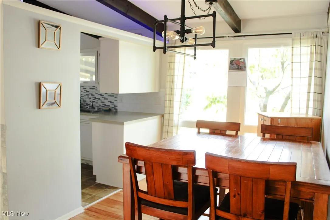 Dining space featuring light wood-style floors, a chandelier, and beamed ceiling