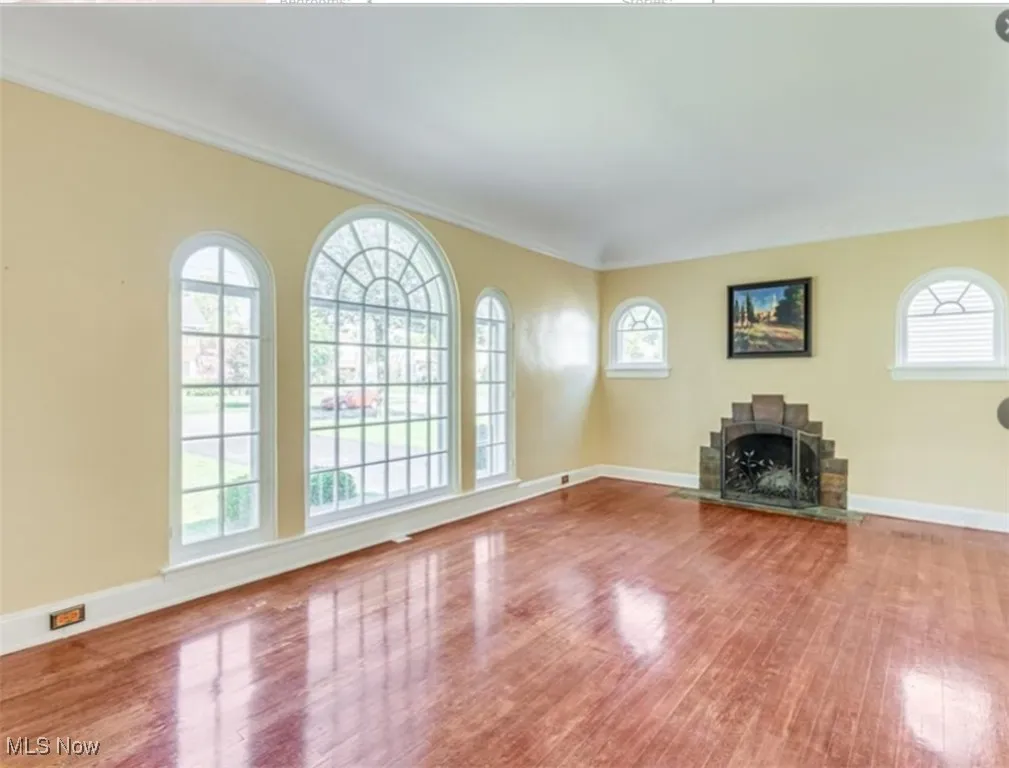 Unfurnished living room featuring wood finished floors, crown molding, and a fireplace with flush hearth