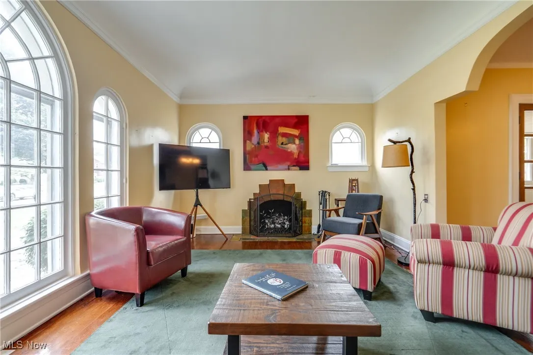 Living area featuring arched walkways, ornamental molding, a fireplace, and wood finished floors