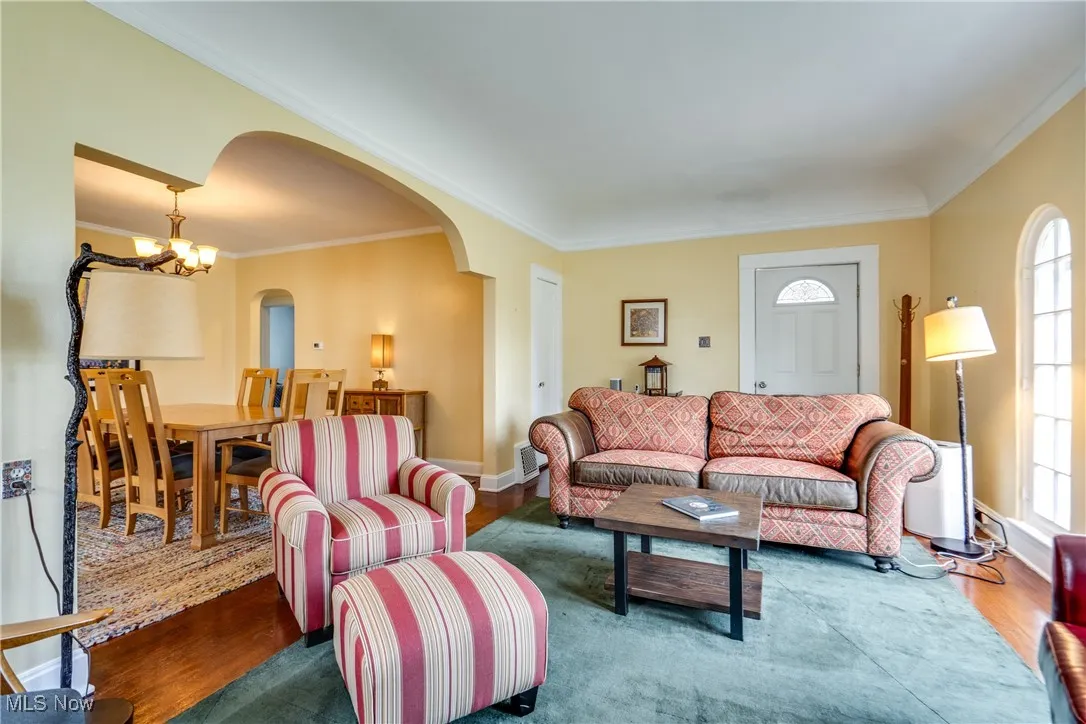 Living room with wood finished floors, crown molding, a chandelier, and arched walkways