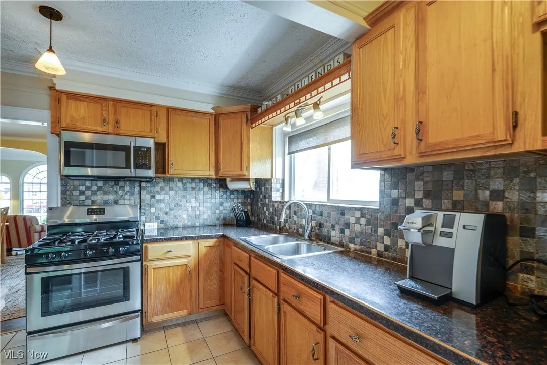 Kitchen with appliances with stainless steel finishes, tasteful backsplash, brown cabinetry, light tile patterned floors, and ornamental molding