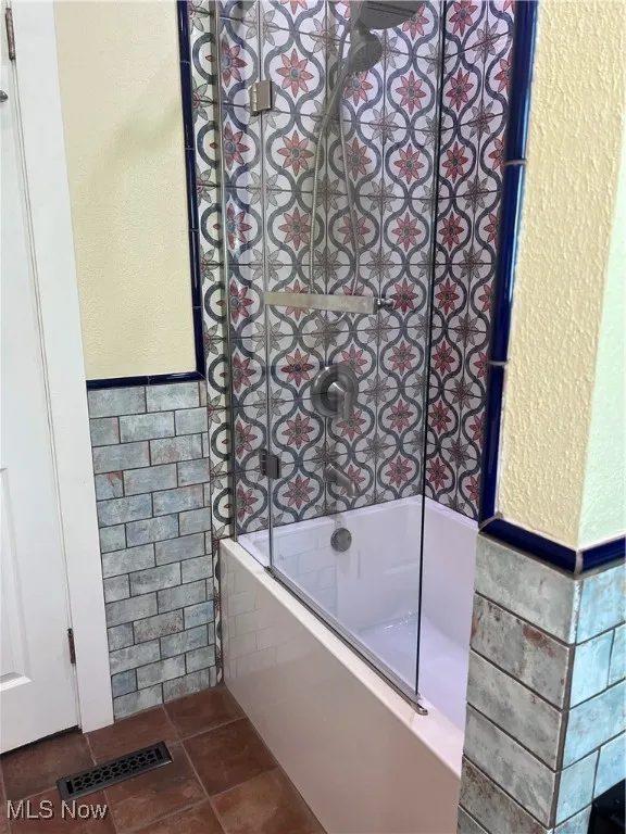 Bathroom featuring tile walls, a textured wall, wainscoting, washtub / shower combination, and dark tile patterned flooring