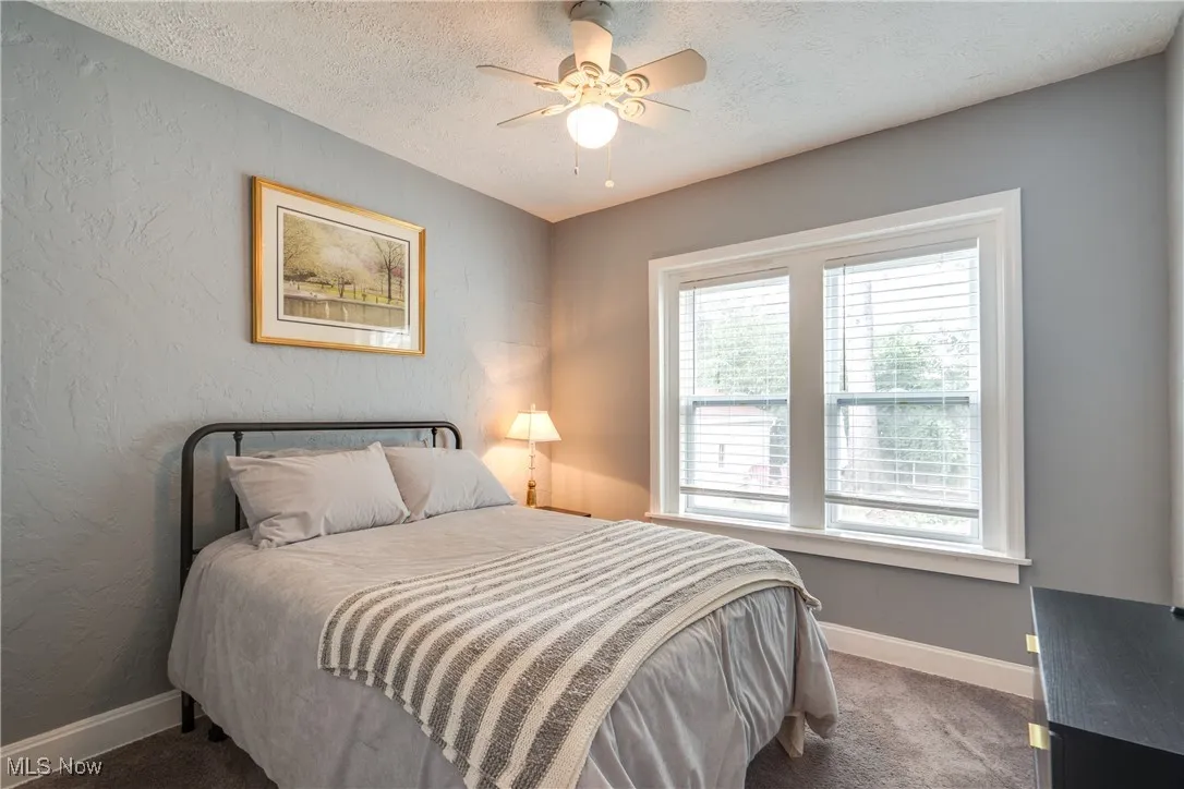 Bedroom with a textured wall, a textured ceiling, a ceiling fan, and dark colored carpet