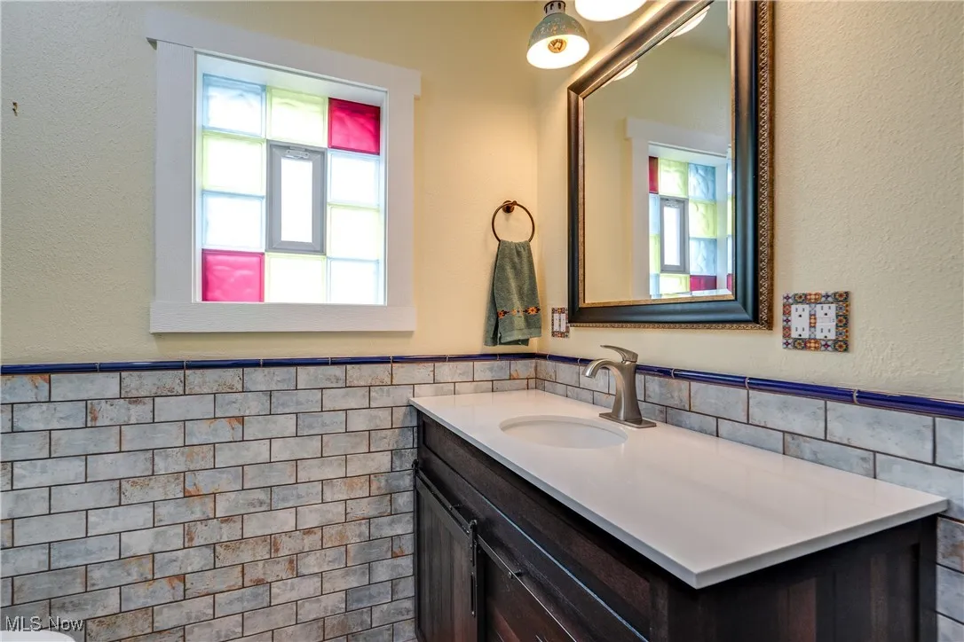 Bathroom featuring a textured wall, tile walls, a wainscoted wall, vanity, and healthy amount of natural light