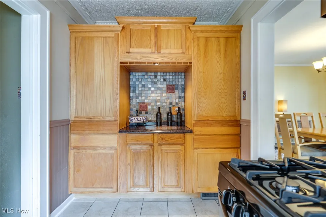 Kitchen with ornamental molding, range with gas cooktop, wainscoting, light tile patterned flooring, and backsplash