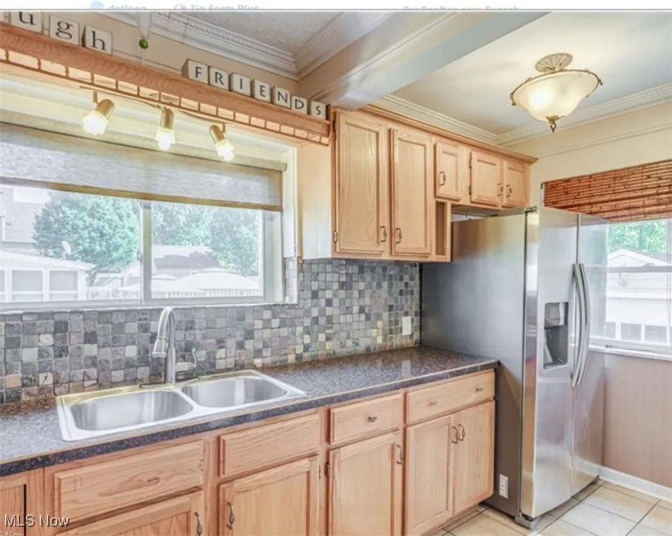 Kitchen with backsplash, dark countertops, stainless steel fridge with ice dispenser, light brown cabinets, and ornamental molding