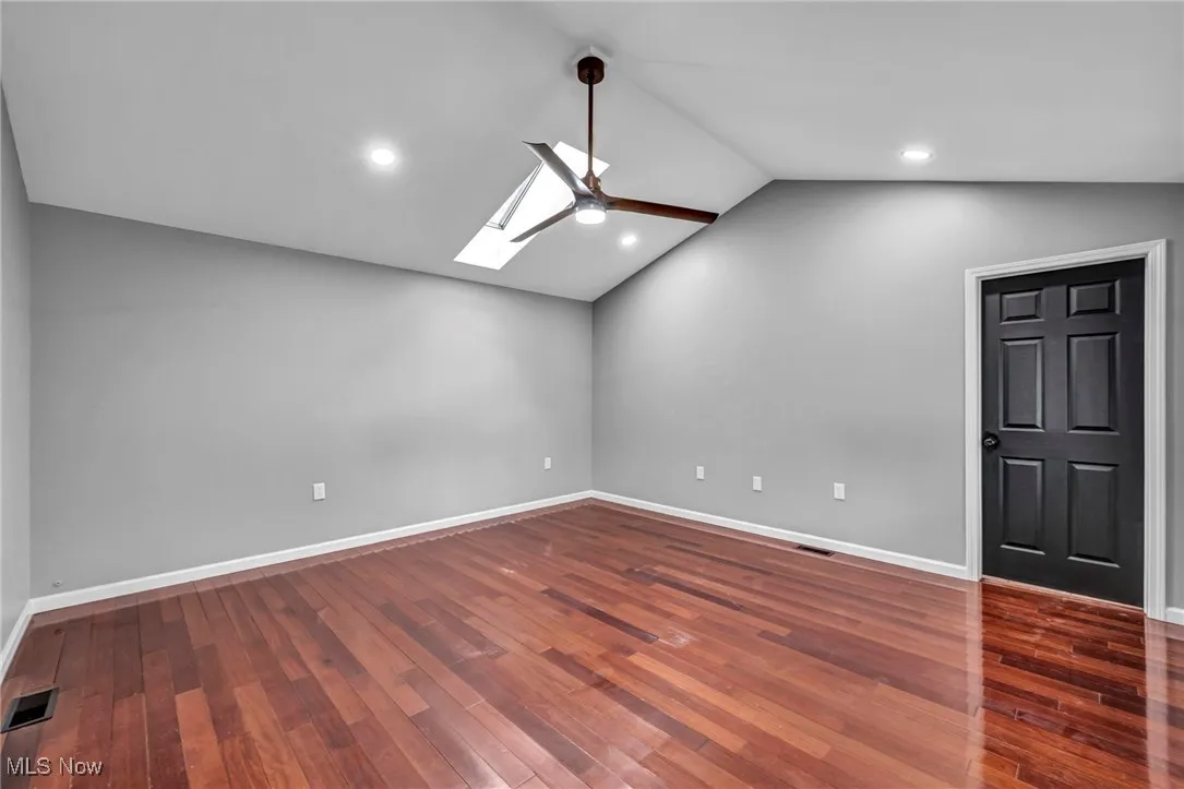 Empty room featuring vaulted ceiling, a skylight, dark wood-style floors, recessed lighting, and ceiling fan