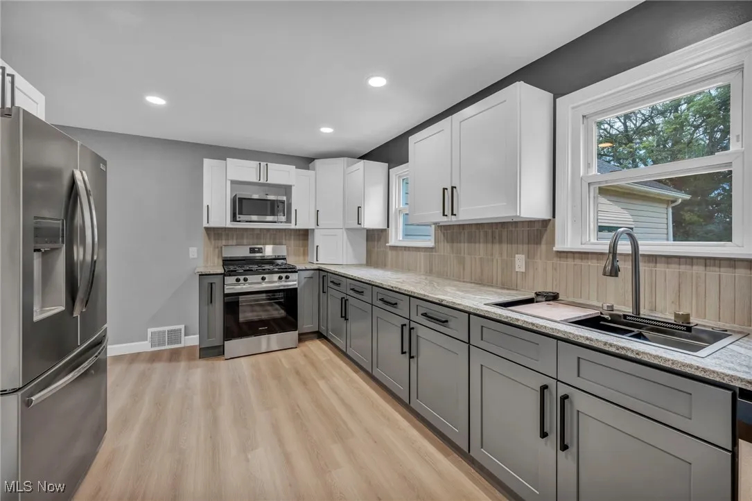 Kitchen with appliances with stainless steel finishes, gray cabinetry, decorative backsplash, white cabinetry, and light wood-style flooring