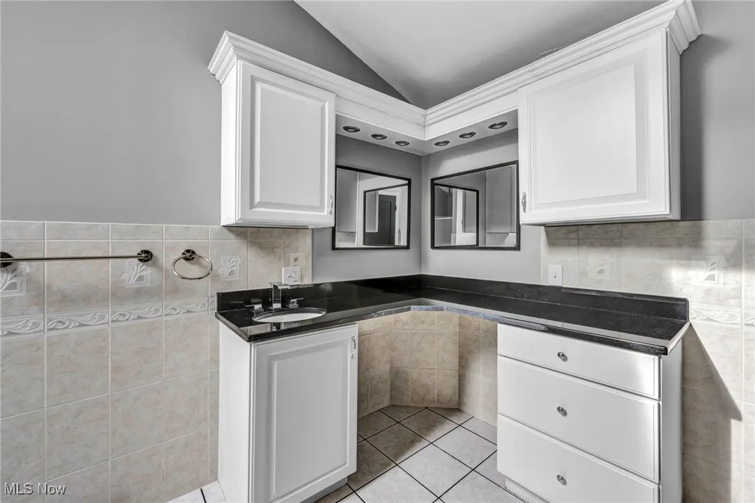 Kitchen with tile walls, white cabinetry, light tile patterned floors, vaulted ceiling, and wainscoting