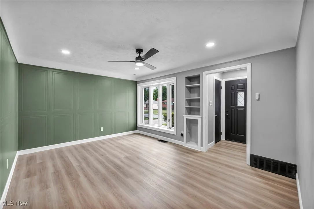 Unfurnished living room featuring built in features, light wood-style flooring, a ceiling fan, a decorative wall, and recessed lighting