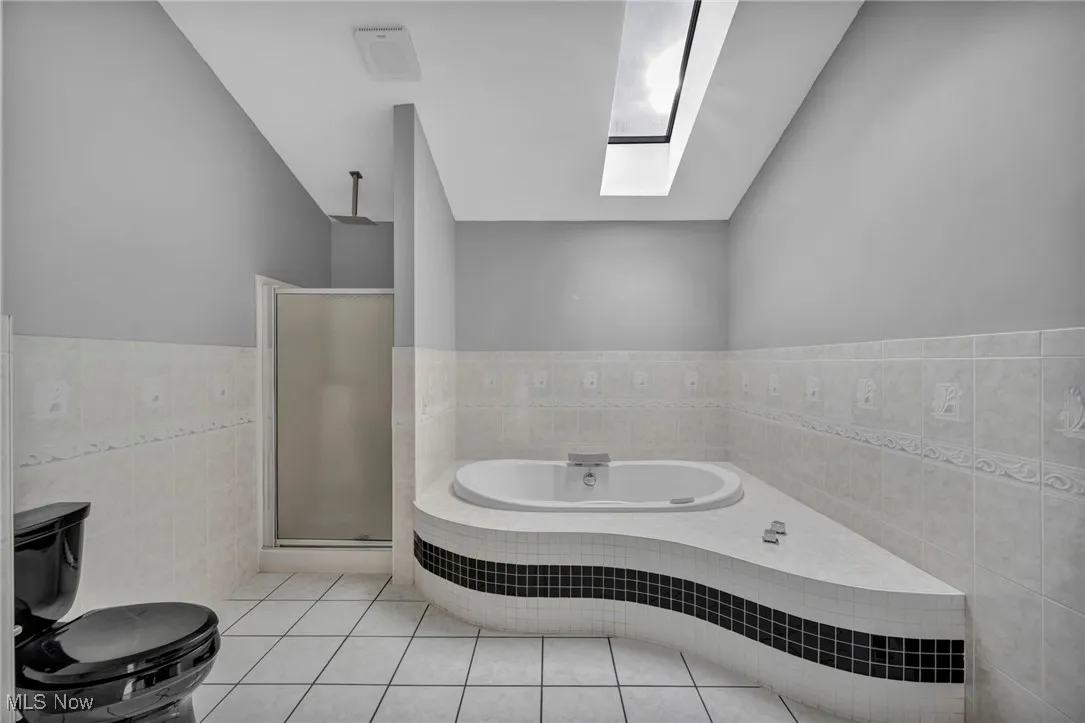 Bathroom featuring tile walls, light tile patterned floors, a bath, a shower stall, and a skylight