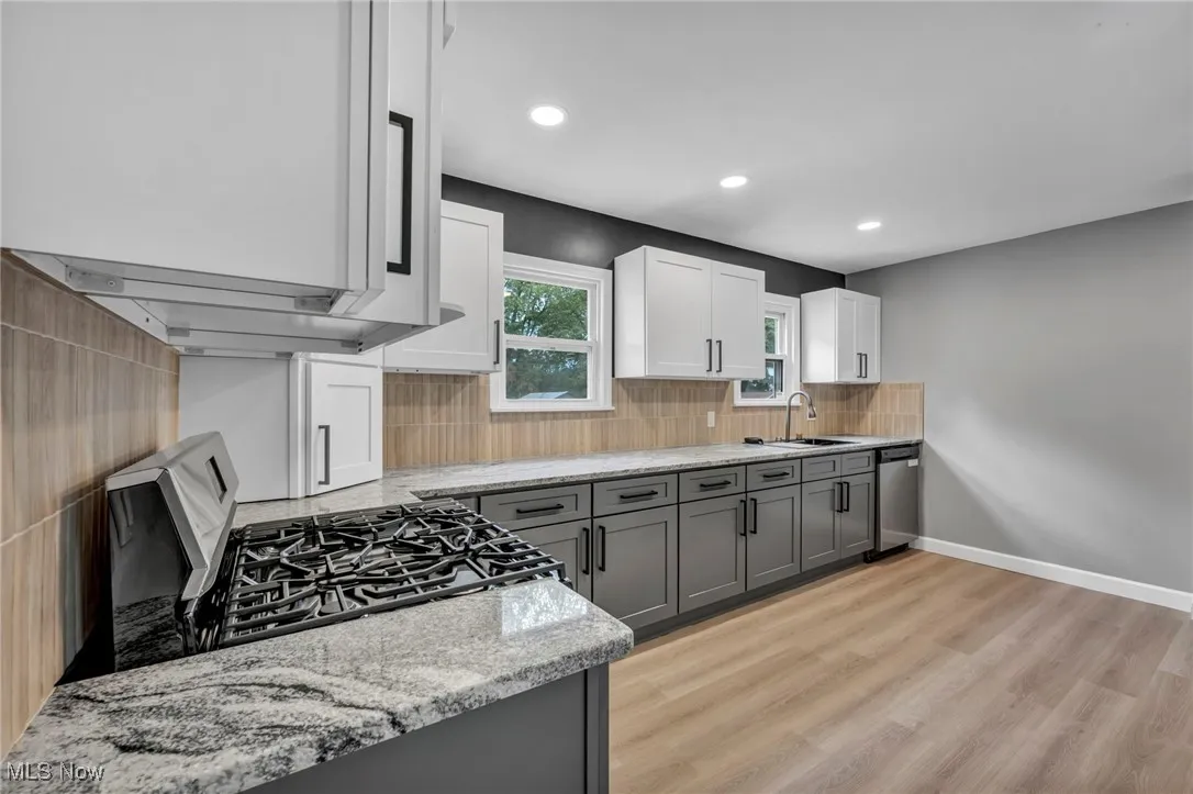 Kitchen with gray cabinetry, light stone countertops, black range with gas cooktop, white cabinetry, and light wood-style flooring