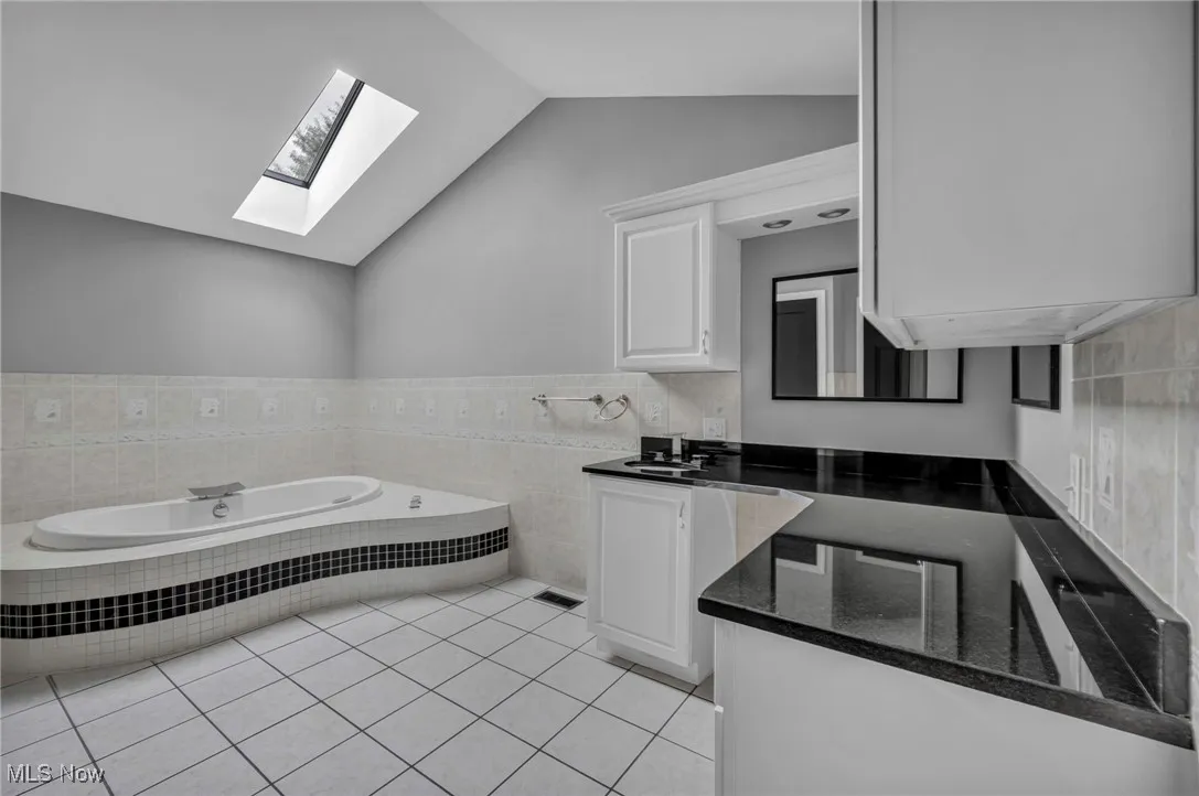 Full bathroom with lofted ceiling, vanity, a bath, light tile patterned floors, and tile walls