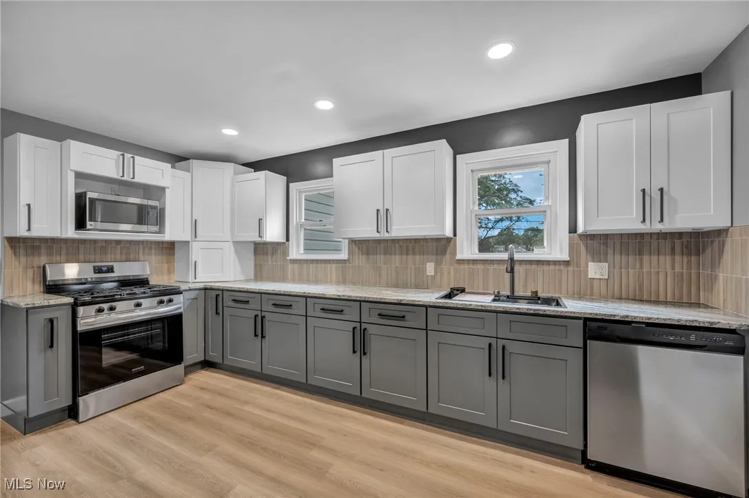 Kitchen with gray cabinets, appliances with stainless steel finishes, backsplash, white cabinets, and light wood finished​​‌​​​​‌​​‌‌​‌‌​​​‌‌​‌​‌​‌​​​‌​​ floors