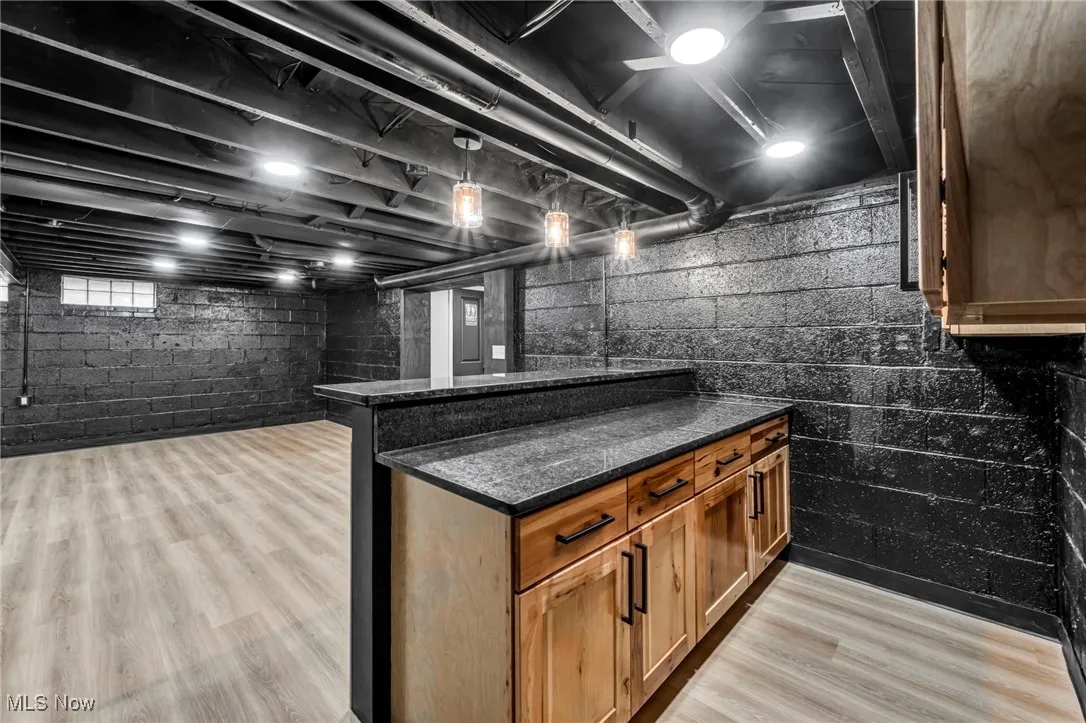 Bar featuring brown cabinets, decorative light fixtures, light wood-type flooring, and dark stone counters