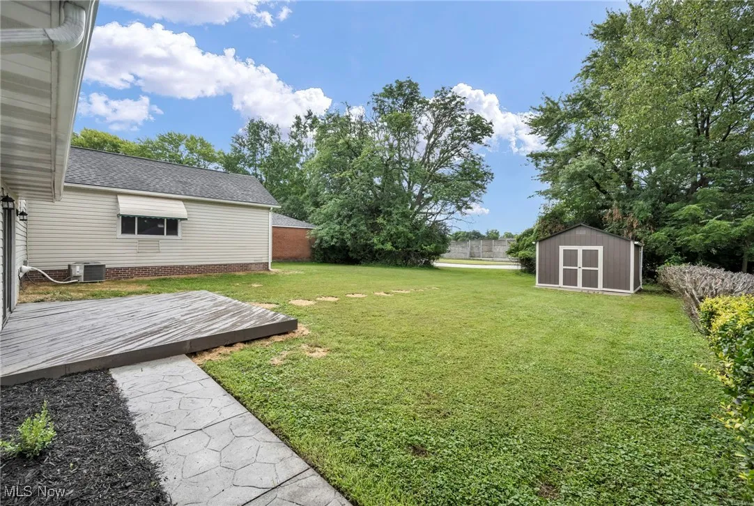 View of green lawn featuring a deck and a shed