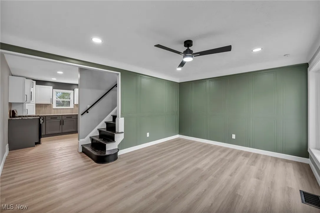 Unfurnished living room with a decorative wall, stairway, light wood-style floors, a ceiling fan, and recessed lighting