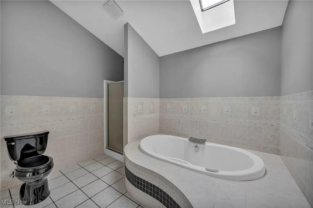 Full bath with a skylight, a garden tub, tile patterned flooring, tile walls, and vaulted ceiling