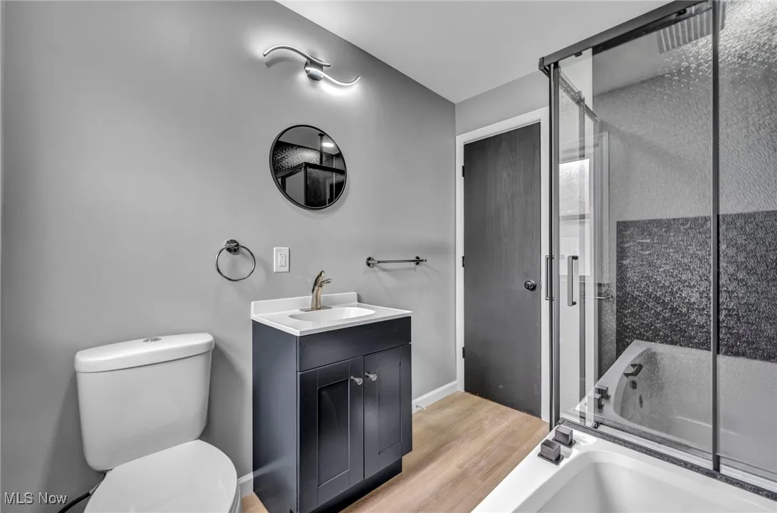 Bathroom featuring light wood-style floors, vanity, and bath / shower combo with glass door