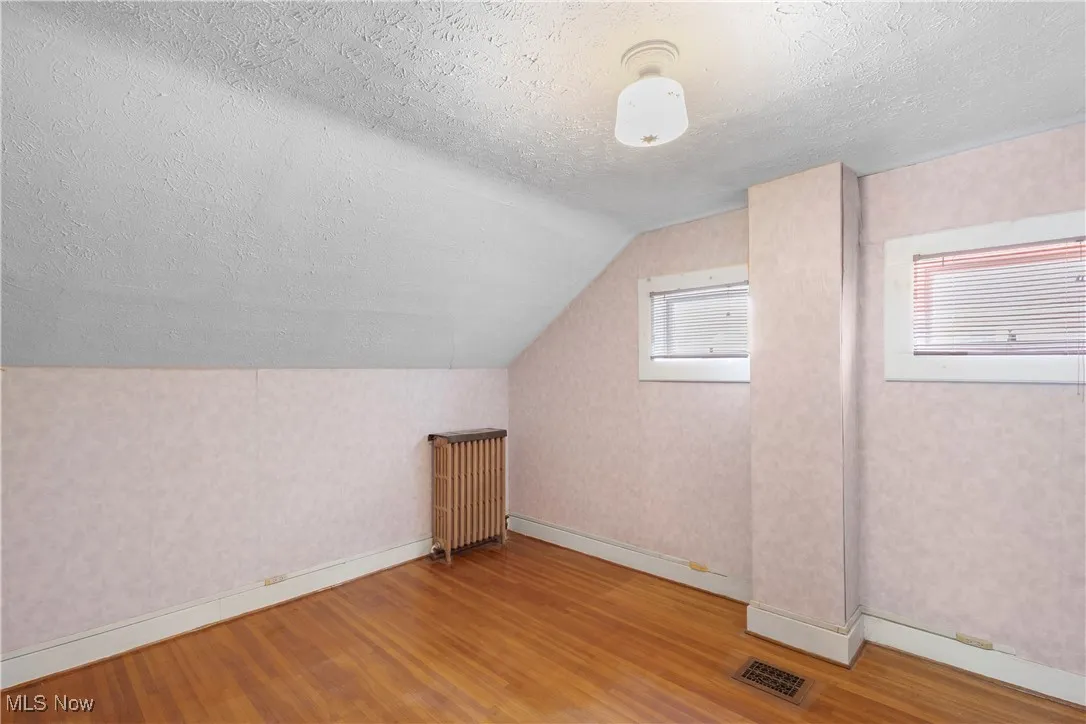 Additional living space with light wood-style flooring, a textured ceiling, radiator heating unit, vaulted ceiling, and wallpapered walls