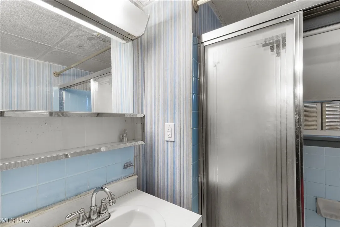 Bathroom featuring wallpapered walls, vanity, a shower, and decorative backsplash