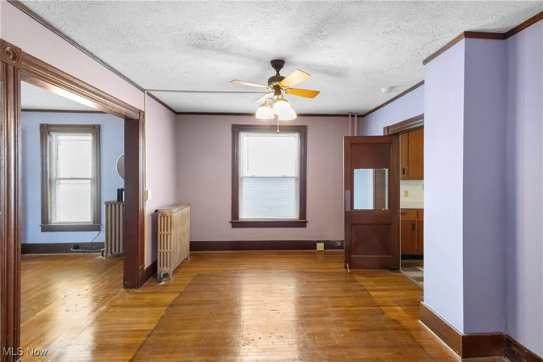 Unfurnished dining area featuring ceiling fan, light wood finished floors, crown molding, radiator, and a textured ceiling