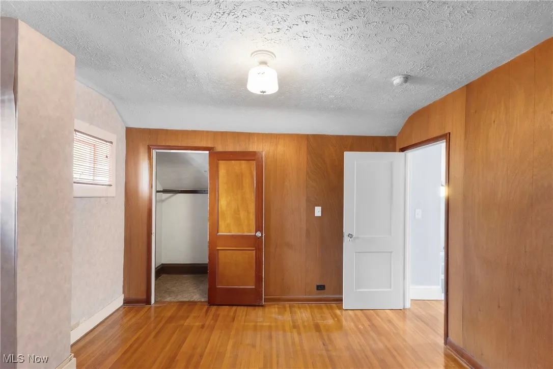 Unfurnished bedroom with a closet, lofted ceiling, wood finished floors, a textured ceiling, and wood walls